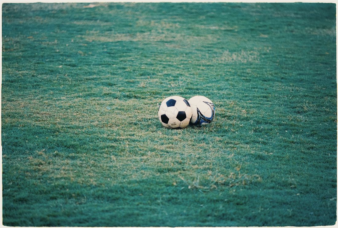 Dua bola sepak tergeletak di rumput lapangan hijau