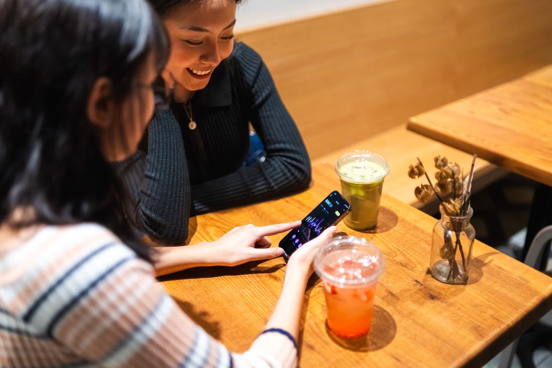 Dua teman melihat aplikasi di ponsel bersama di kafe